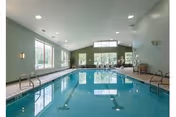 Indoor swimming pool in a bright room with large windows, lounge chairs, and a vaulted ceiling.
