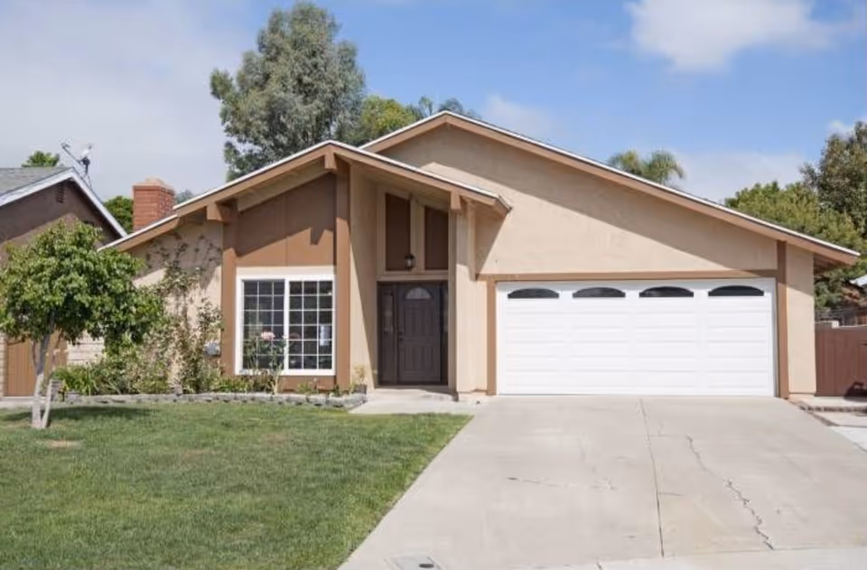 A single-story beige house with a two-car garage and front lawn.