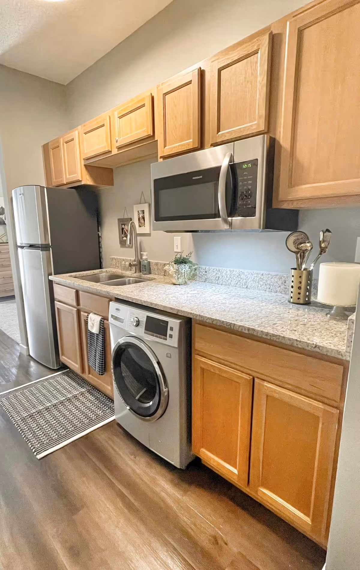 Kitchenette with wood cabinets, granite countertop, stainless microwave and refrigerator, sink and a front-loading washer under the counter.