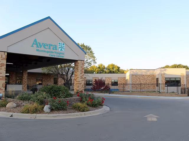 Front entrance and covered porte-cochère of Avera Morningside Heights Care Center with a roundabout driveway, landscaping, and brick building in the background.