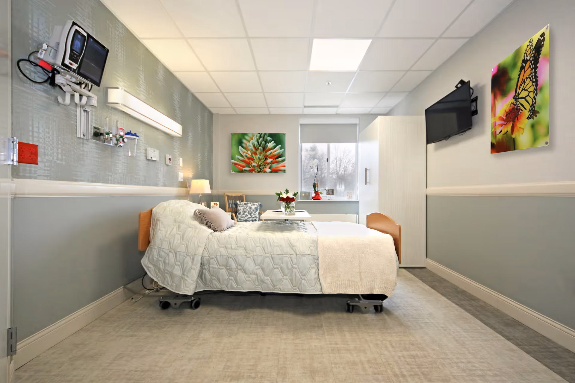 A bright, modern nursing home patient bedroom with a single bed, wall-mounted TV, medical equipment, and decorative artwork.