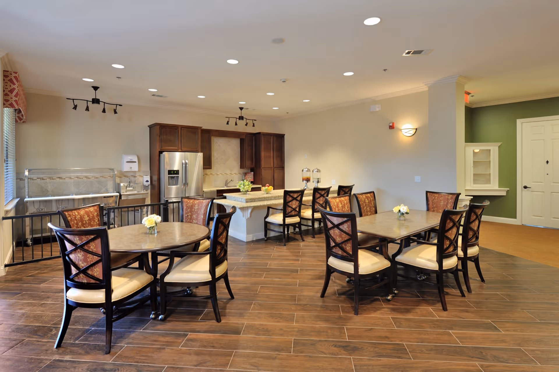 Open dining and kitchenette area with several tables and chairs, a central island, and a stainless-steel refrigerator.