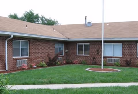Exterior view of a single-story brick senior facility with a green lawn and walkway.