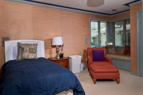 Bedroom with a navy blue comforter on the bed, red chaise lounge, and window seating.