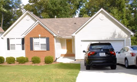 Single-story suburban brick-and-siding house with an attached garage, two cars in the driveway, and a grassy front lawn.