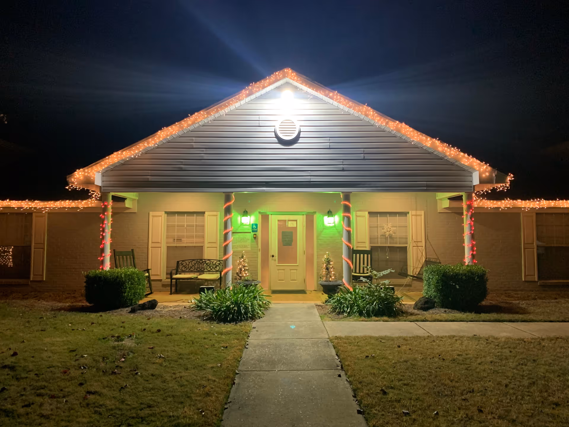 Front entrance of a single-story building decorated with Christmas lights at night.