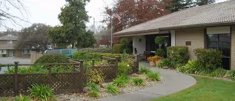 Exterior view of a senior living facility entrance with curved walkway and landscaping.