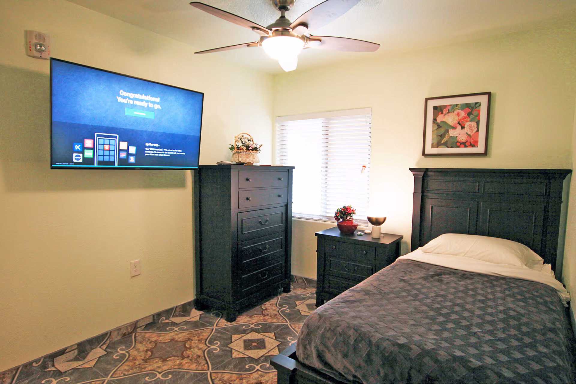 Cozy bedroom with dark wood bed, dresser, nightstand, and wall-mounted TV.