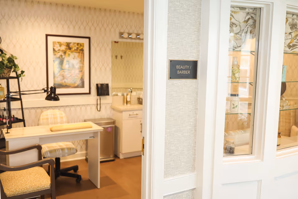 Interior view of a beauty/barber salon area with a manicure table, chairs, and a 'Beauty / Barber' sign on the wall.
