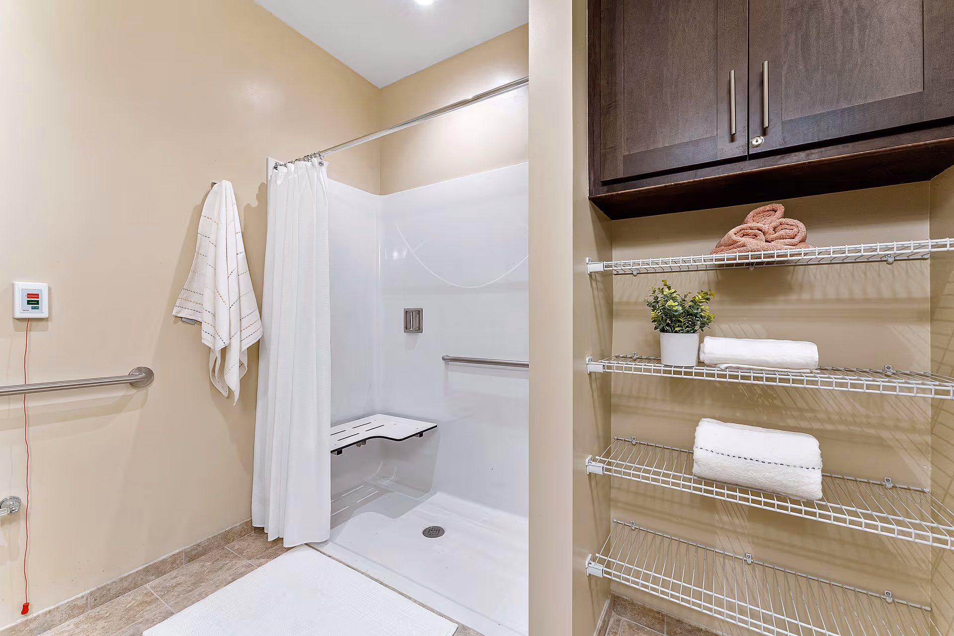 Accessible bathroom with a walk-in shower and folding seat, shower curtain, grab bars, shelving with towels and a cabinet.