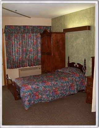 Bedroom with floral bedspread, dark wooden wardrobe, dresser, and green paneled walls.