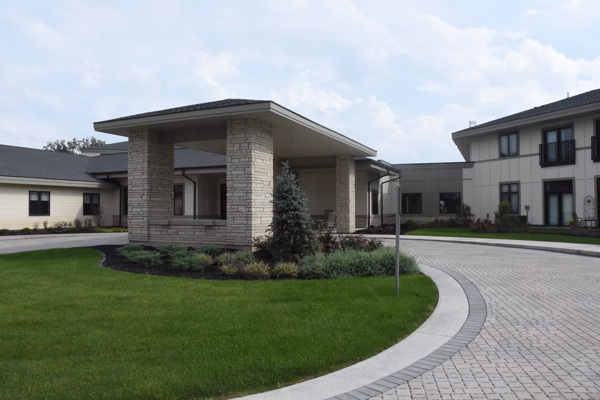 Entrance porte-cochere and landscaped circular driveway in front of a senior living facility building.