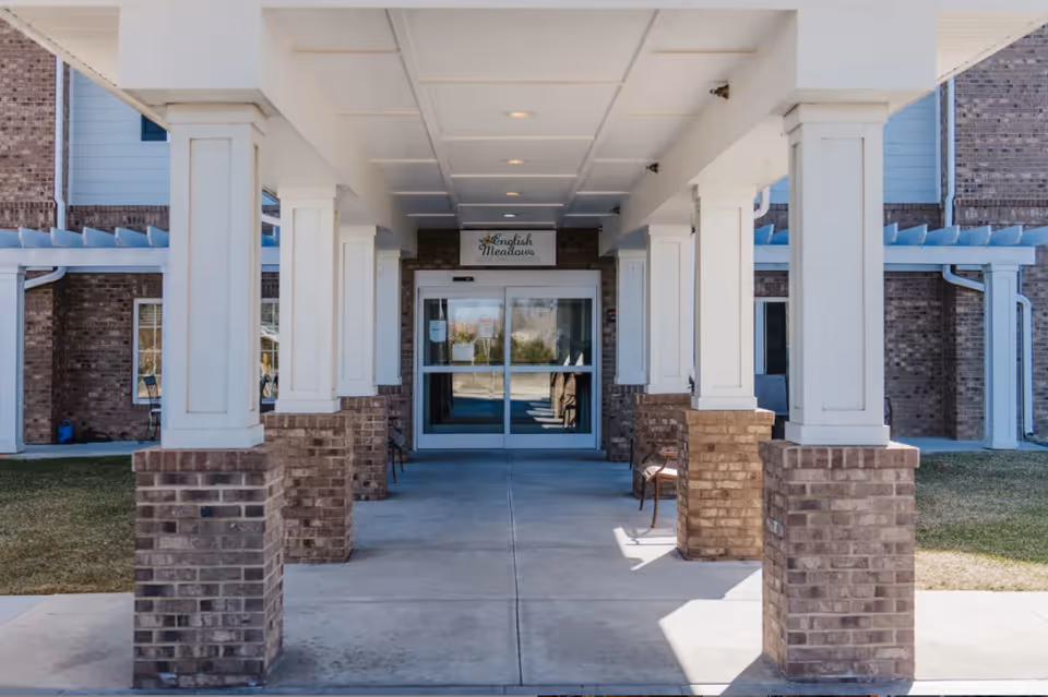 Covered entrance walkway with brick and white columns leading to glass automatic doors of the English Meadows Stephens City Campus building.