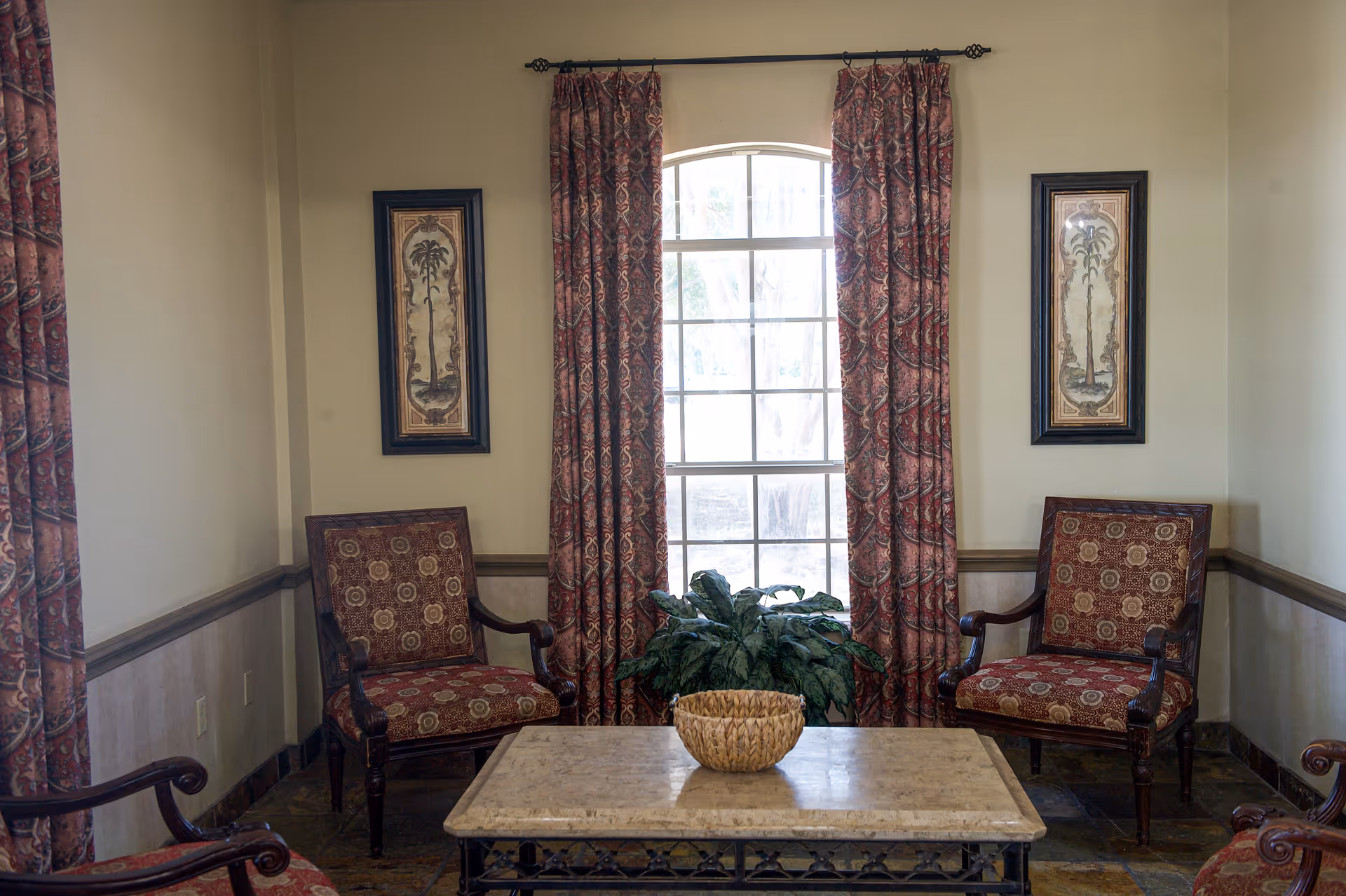 Seating area with two upholstered armchairs beside a tall window, patterned curtains, a coffee table and a decorative basket.