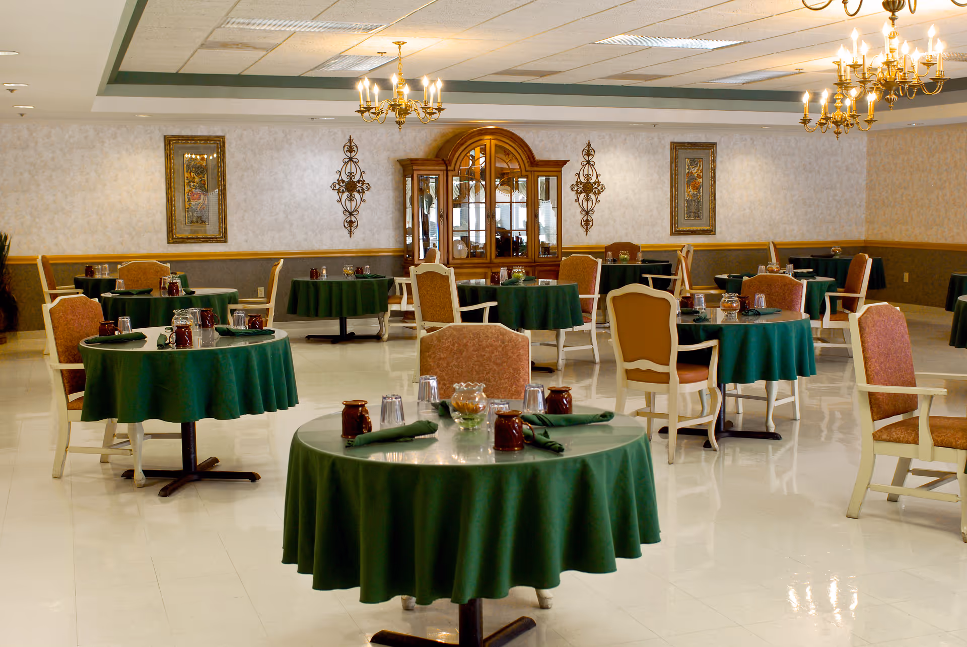 Spacious dining room with round tables covered in green tablecloths and chairs set for meals.