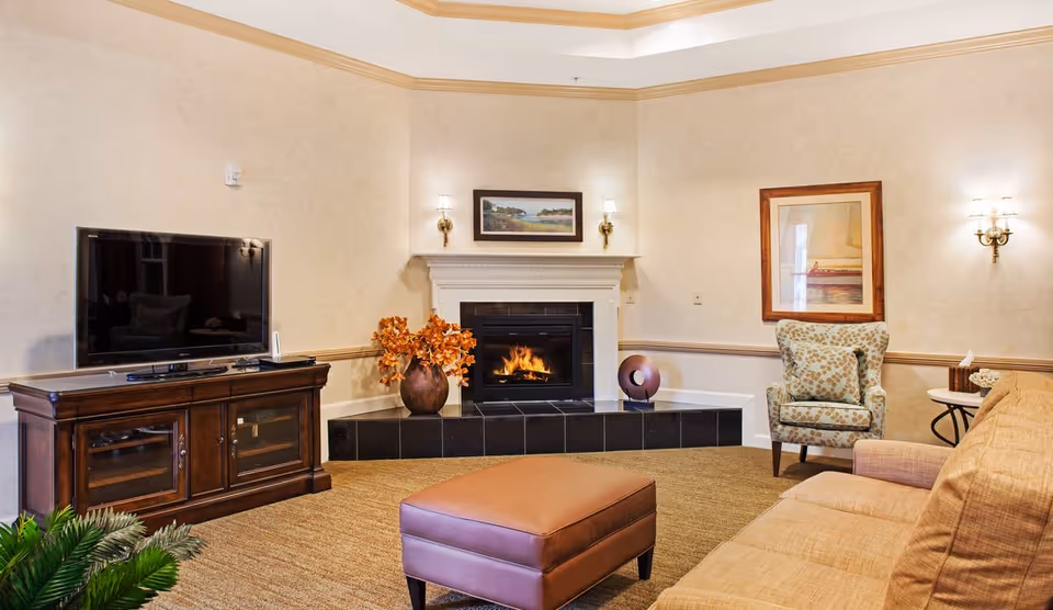 Cozy sitting area with a lit fireplace, flat-screen TV on a wooden cabinet, sofa, armchair, and ottoman.