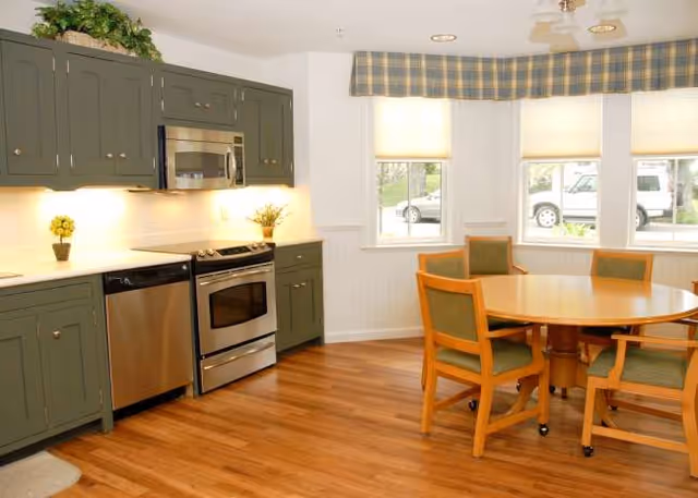 A kitchen and dining area with green cabinets, stainless appliances, and a round table.