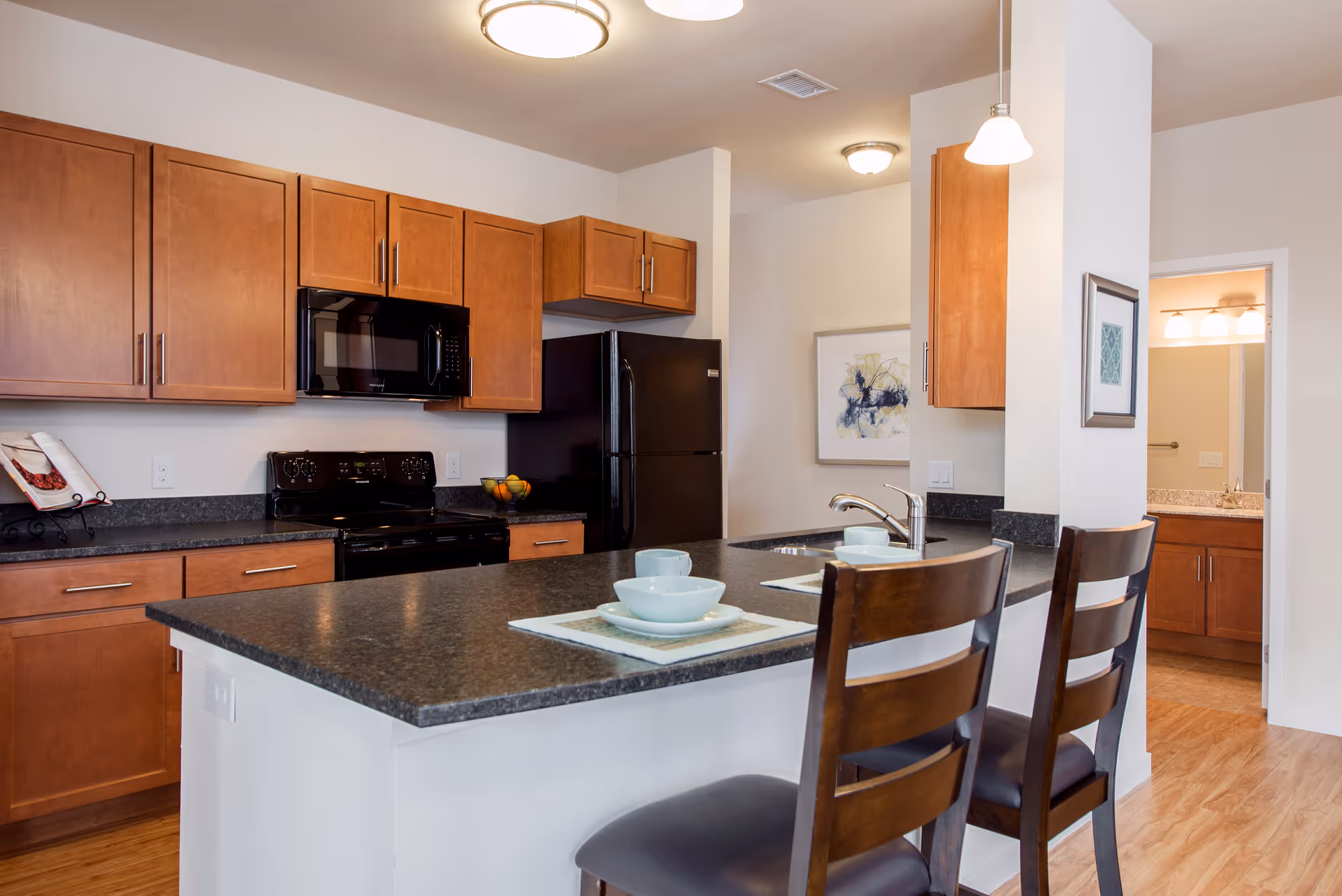 Modern open kitchen with wood cabinets, black appliances and a large island with two bar stools and place settings.