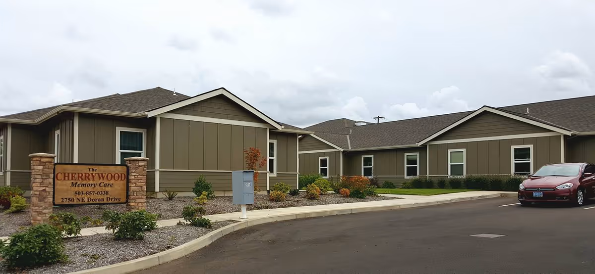 Exterior view of Cherrywood Memory Care facility with sign, beige siding, and a parked car.