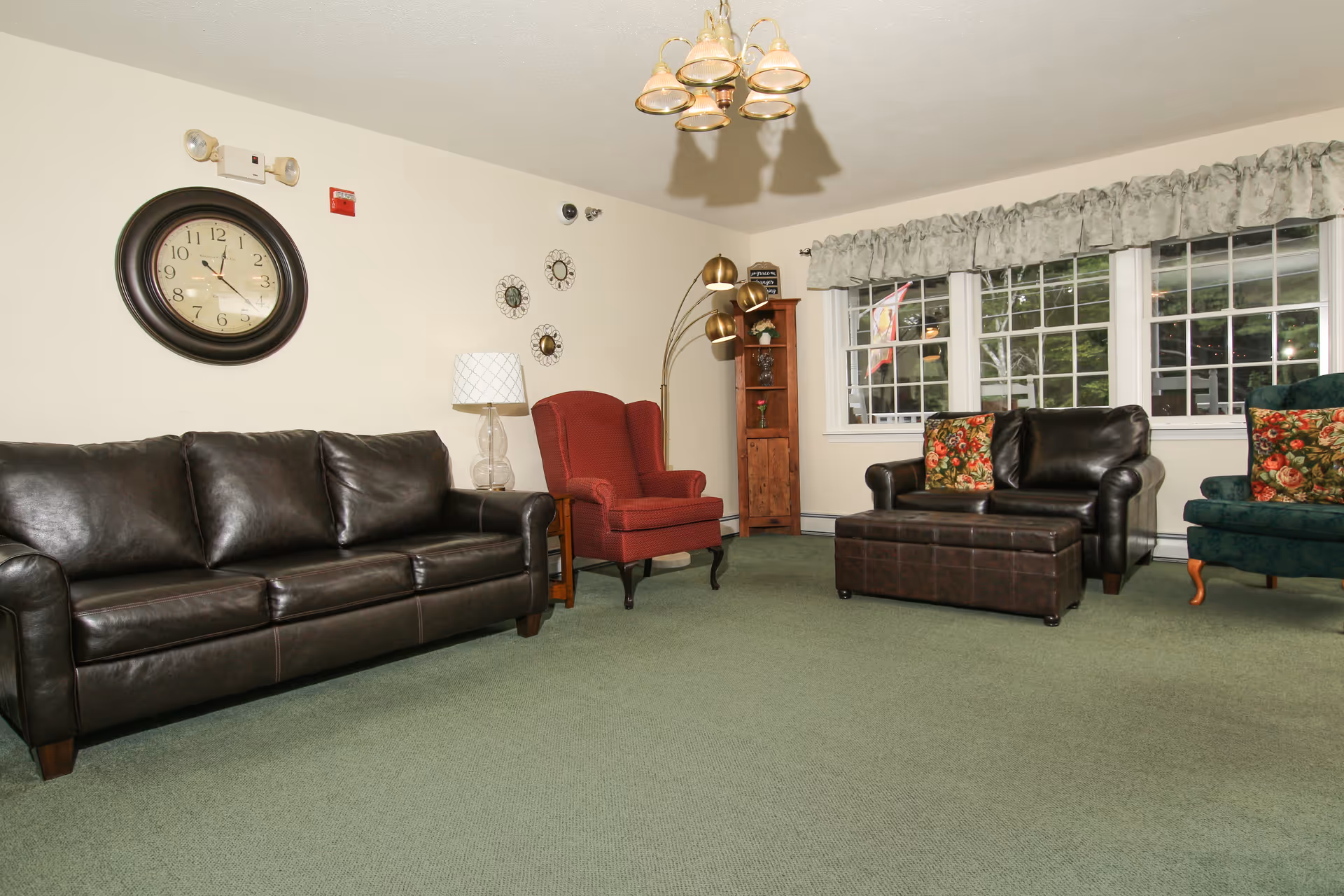 Spacious lounge with leather sofas, armchairs, ottoman, wall clock and large windows.
