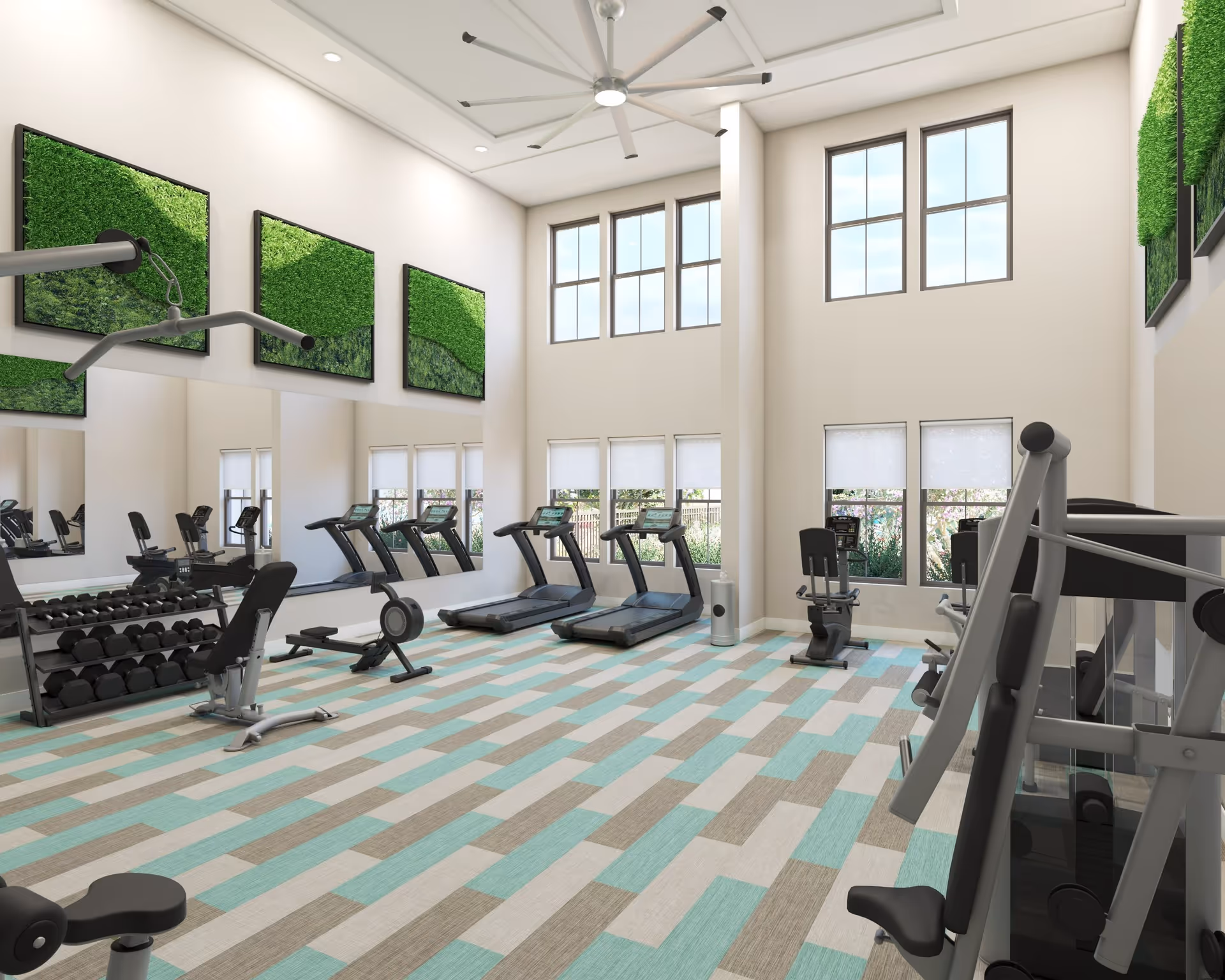 A bright and spacious fitness room with large windows letting in natural light. The room features several treadmills, a recumbent bike, weight machines, and a rack of dumbbells. The walls are decorated with green moss art panels, and there is a large ceiling fan overhead. The floor has a patterned carpet in shades of blue, beige, and gray.