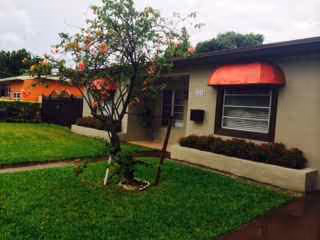 A single-story building with red awnings, green lawn, and a tree at the front.