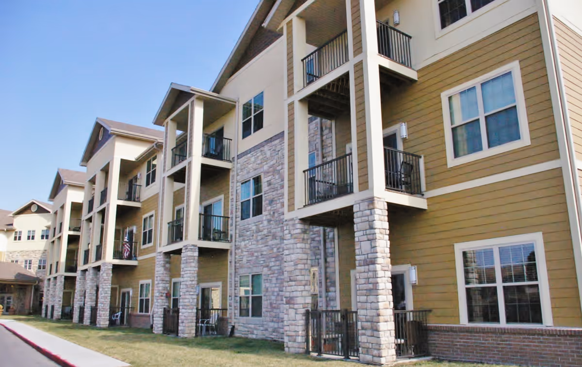 Exterior view of a multi-story senior living building with balconies and stone columns.