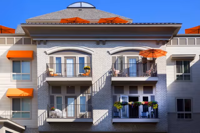 Facade of a multi-story residential building with balconies, orange awnings and umbrellas, and potted plants.