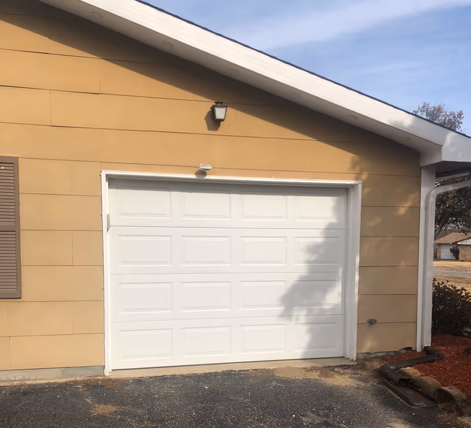 Beige building exterior with a white garage door and outdoor light.