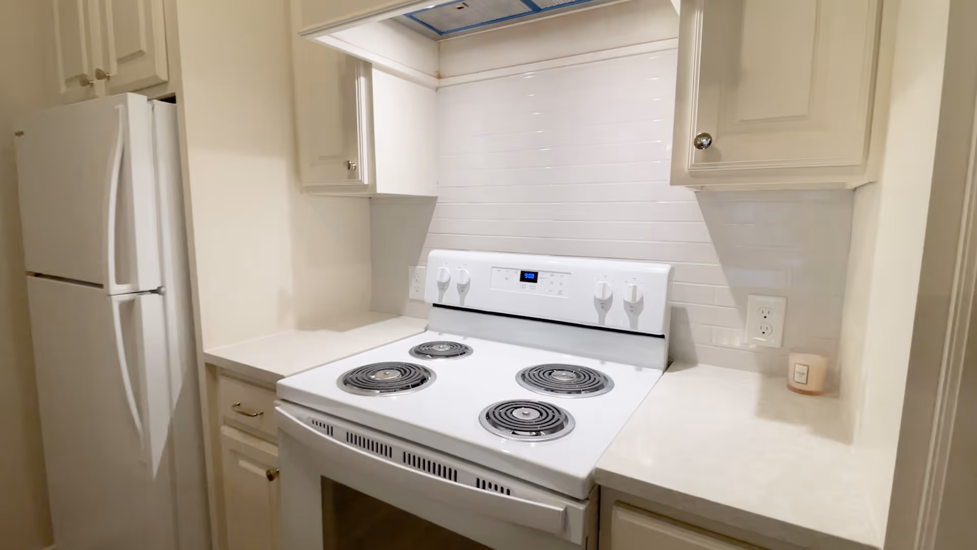 Small white kitchen featuring an electric stove with four coil burners, white cabinets, countertops, and a refrigerator.