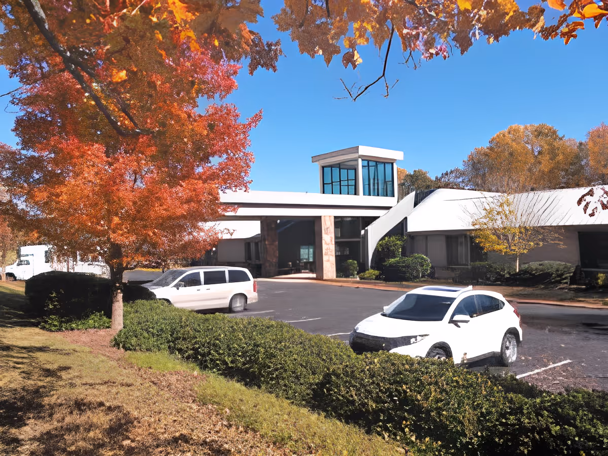 Exterior view of TerraBella Summit facility with a modern building featuring large windows and a covered entrance. There are two white vehicles parked in front, surrounded by autumn trees with vibrant orange and red leaves under a clear blue sky.