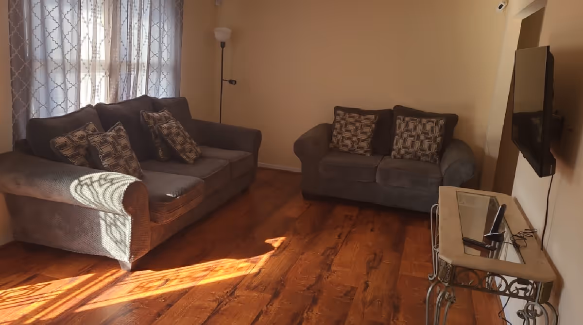 Cozy living room with two gray sofas, sunlight on wood floor, wall-mounted TV.