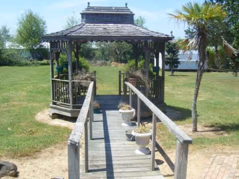 Wooden gazebo at end of ramped walkway with potted plants in a grassy yard.