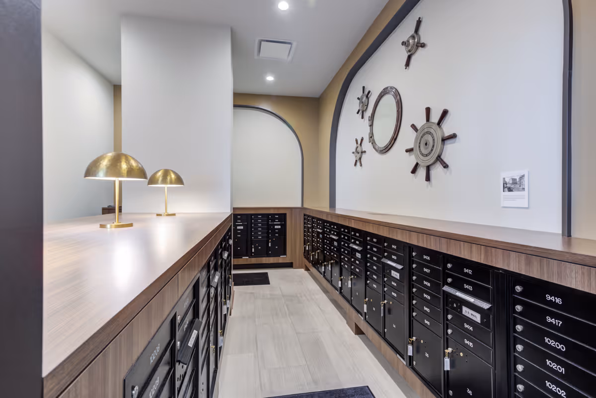 Mailroom with rows of black numbered mailboxes under a wooden counter, brass lamps on the countertop, and decorative ship wheels on the wall.