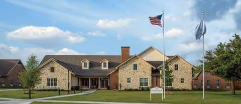 Front exterior of Sonoma House Assisted Living building with flagpoles and lawn.