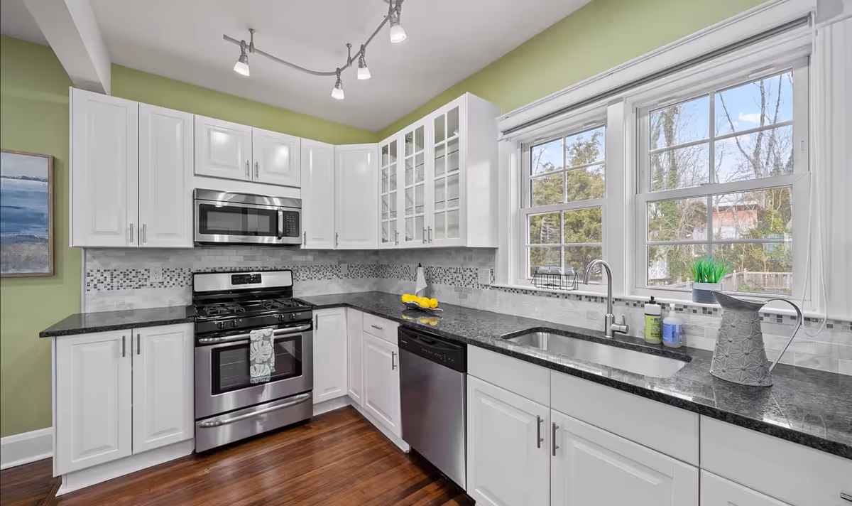 Bright white kitchen with stainless appliances, granite counters, and large windows.