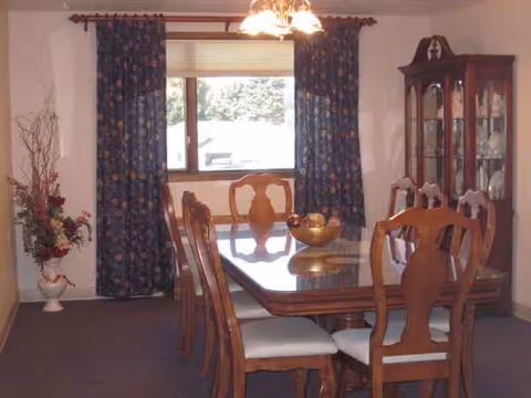 Senior living dining room with a wooden table, chairs, and china cabinet under a chandelier.