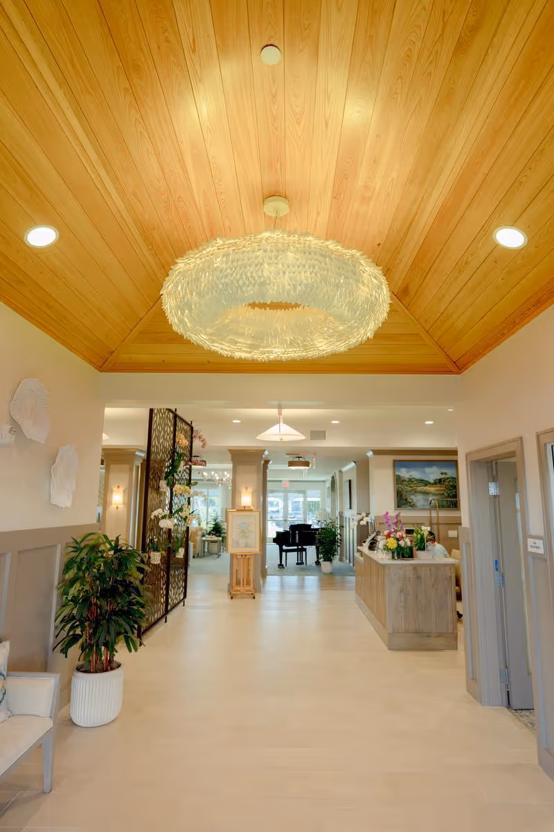 Bright lobby interior with a wooden vaulted ceiling, large decorative chandelier, reception desk and a piano in the background.