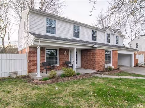 Two-story brick and siding house with a small front porch and chairs.