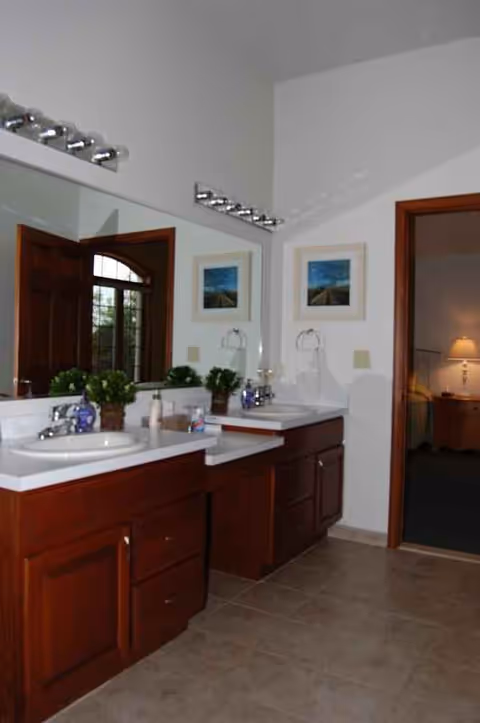 Double-sink bathroom vanity with mirrors, cabinets, and adjacent bedroom doorway.