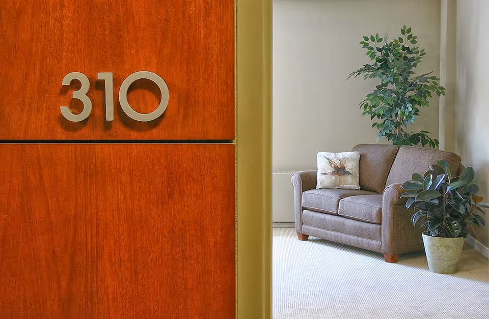 A close-up view of an apartment door with the number 310 and a glimpse of a cozy living area featuring a brown sofa and plants.