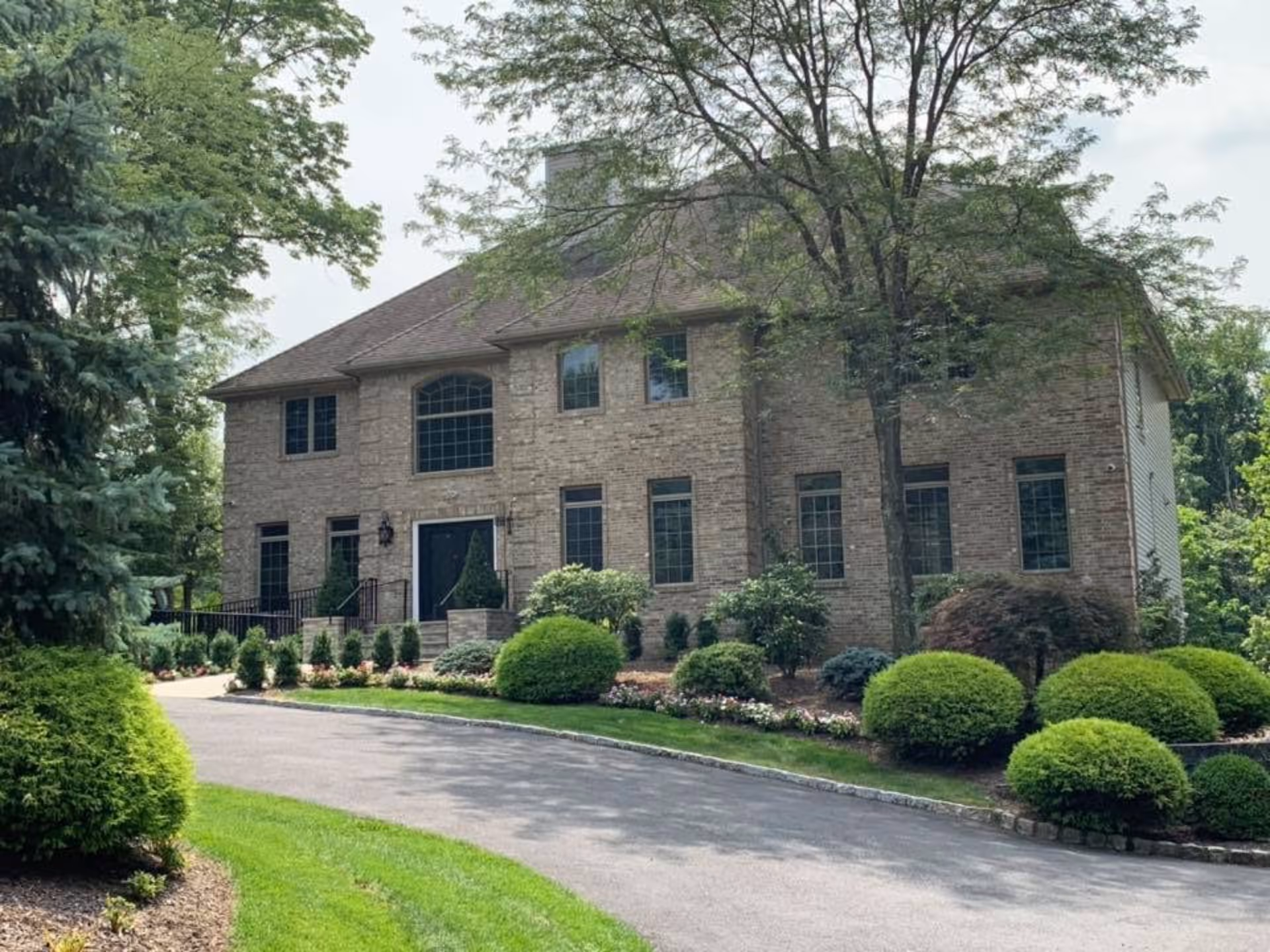 Exterior view of a large two-story brick building surrounded by well-maintained landscaping including bushes, trees, and a curved driveway leading to the entrance.