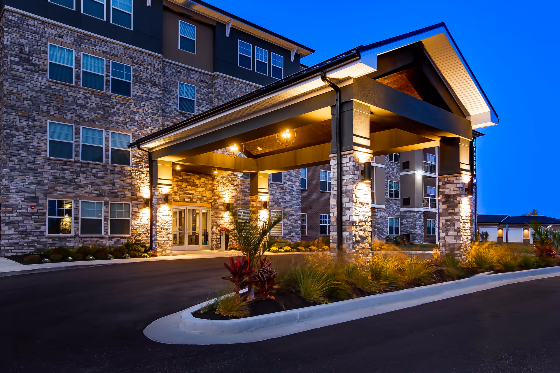 A modern apartment building front with stone columns and a lit entryway at dusk.