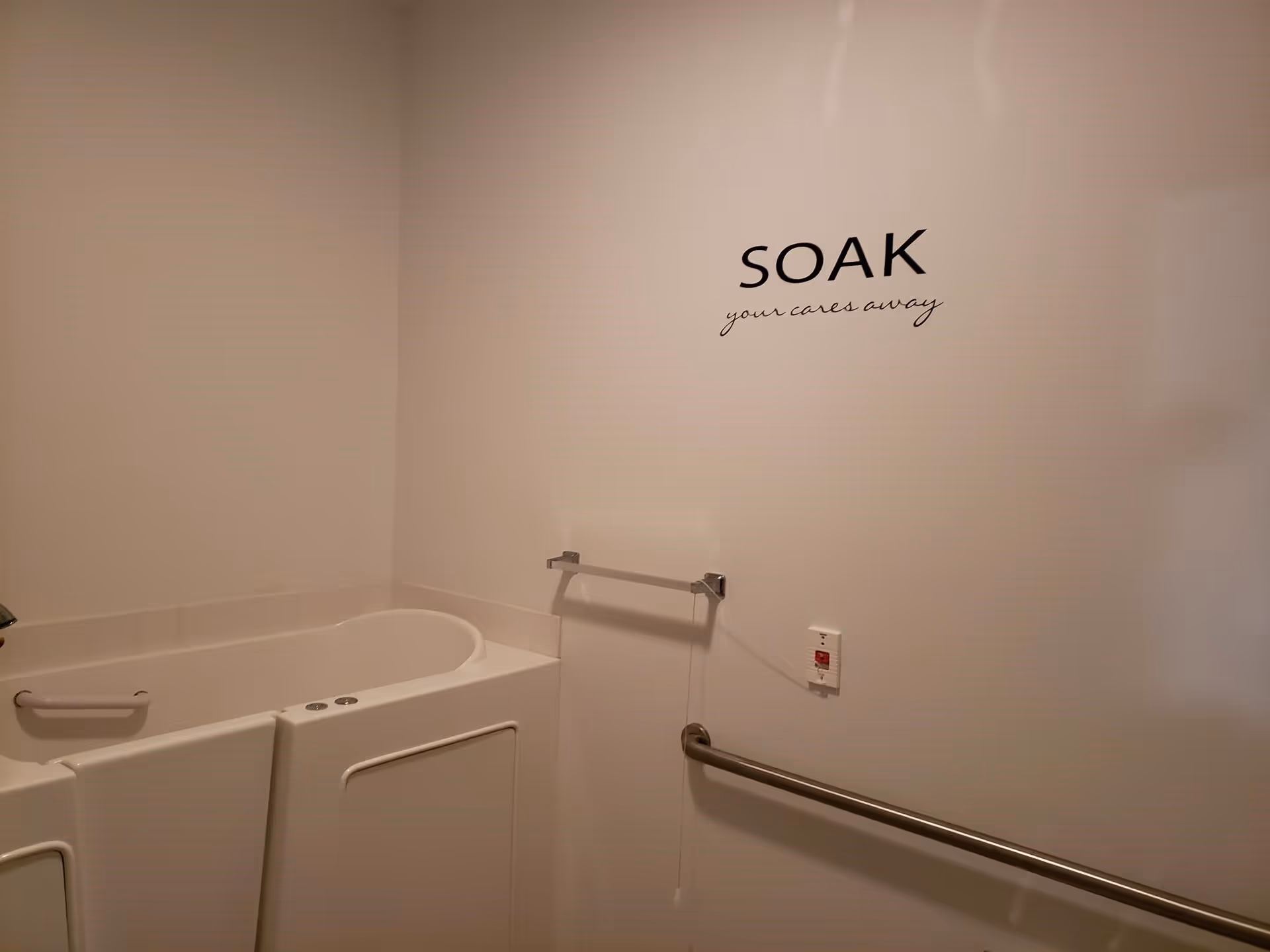 Walk-in bathtub with grab bars and a wall decal reading 'SOAK your cares away'.