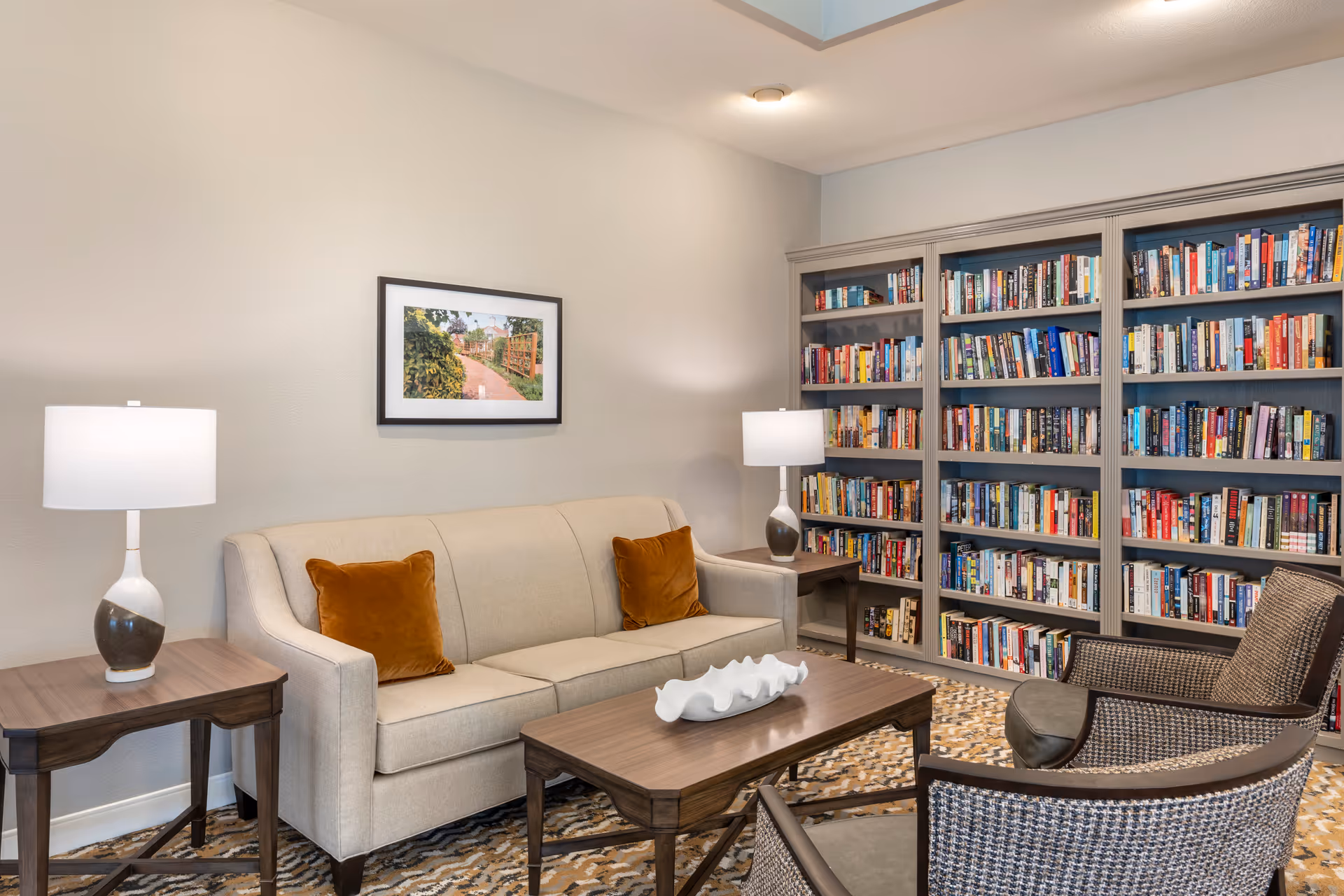 Cozy seating area with a sofa, armchairs, coffee table, lamps, and built-in bookshelves filled with books.