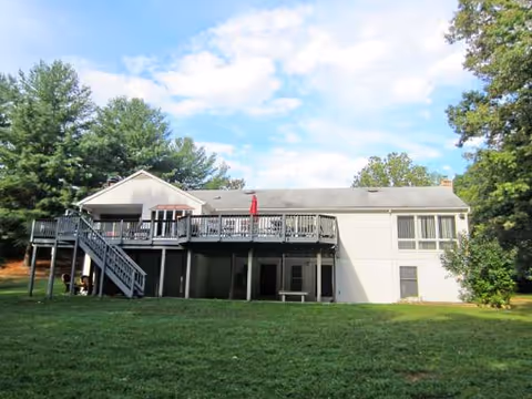 Exterior view of a two-story senior living building with deck, lawn, and trees.