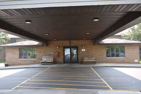 Brick senior living facility entrance with a covered drop-off and benches.