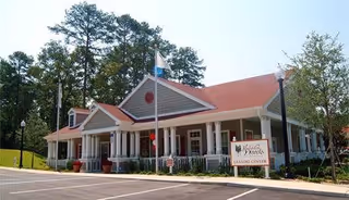 Exterior view of a single-story building with a red roof and white columns, surrounded by trees and a parking lot. A sign in front reads 'Jamestown Woods Learning Center.'