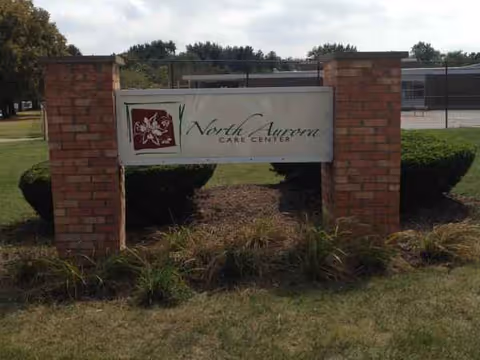 Outdoor sign for North Aurora Care Center between brick pillars on the lawn.