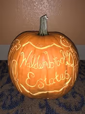A carved pumpkin sitting on patterned carpet against a wall engraved with 'Waldenbrook Estates'.